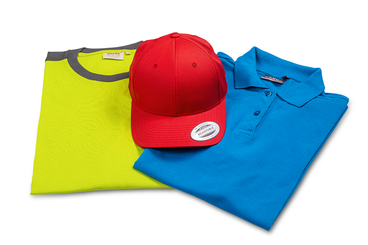 Rotes Baseball-Cap liegt auf grünem Shirt mit grauem Rundhalsausschnitt sowie einem blauen Poloshirt
