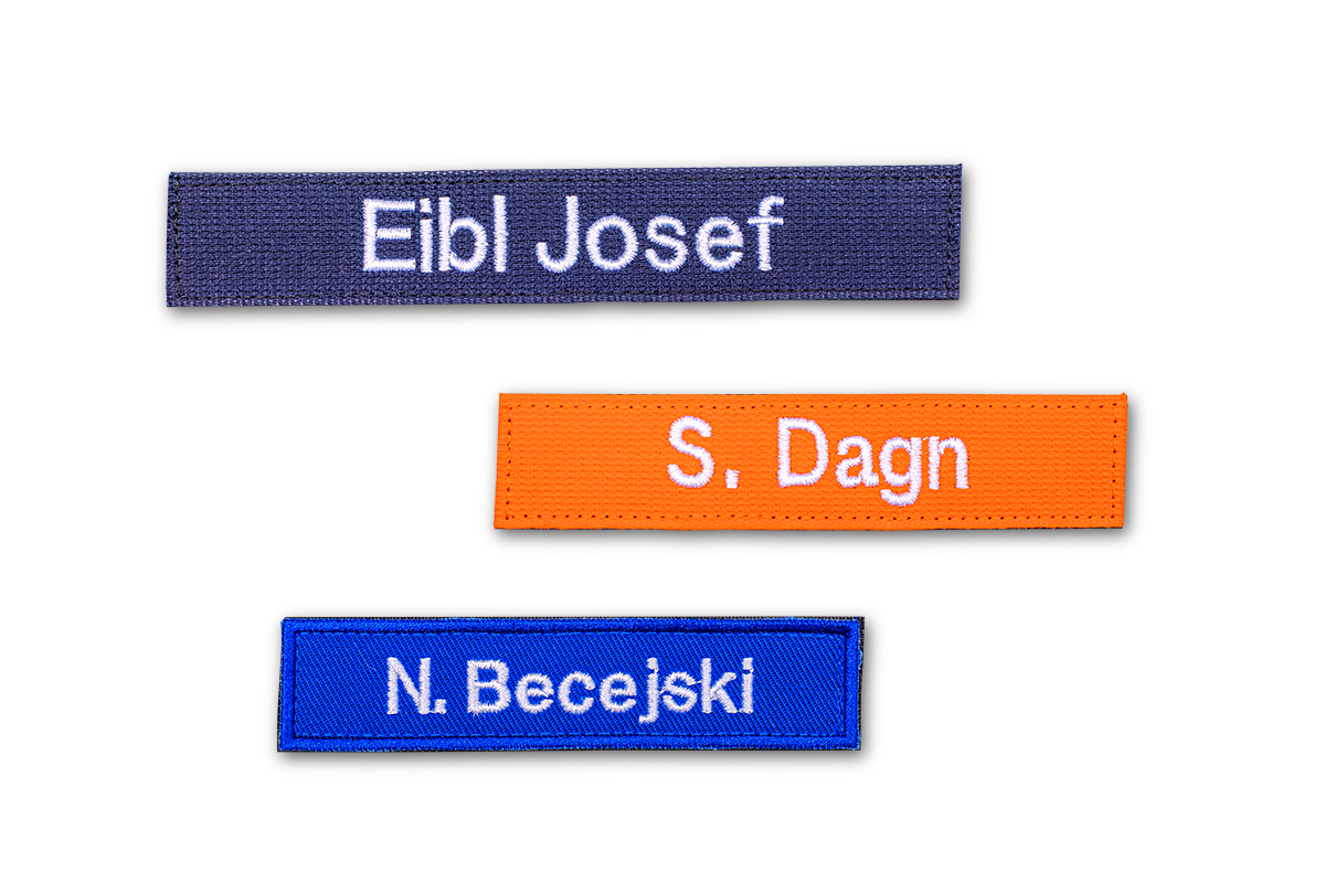 Dunkelblaues Namensabzeichen mit der Aufschrift Eibl Josef, oranges Namensabzeichen mit der Aufschrift S. Dagn, mittelblaues Namensabzeichen mit der Aufschrift N. Becejski