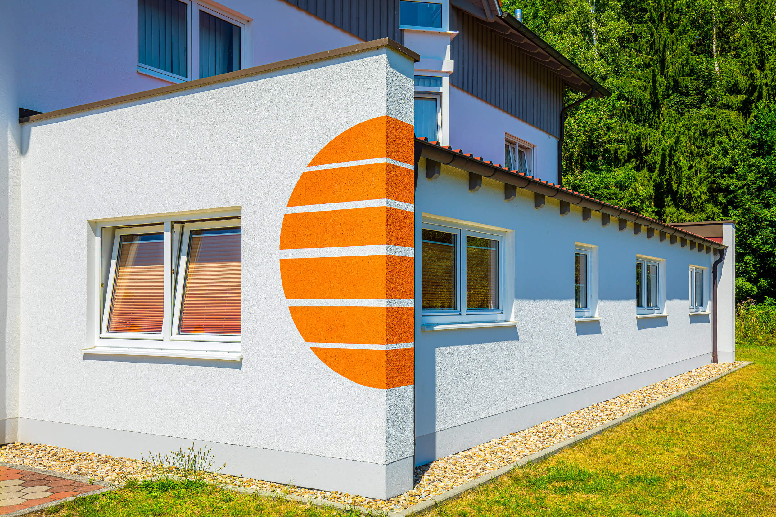 Seitenansicht des Hauses mit Anbau und orangen Streifen in Form einer Sonne